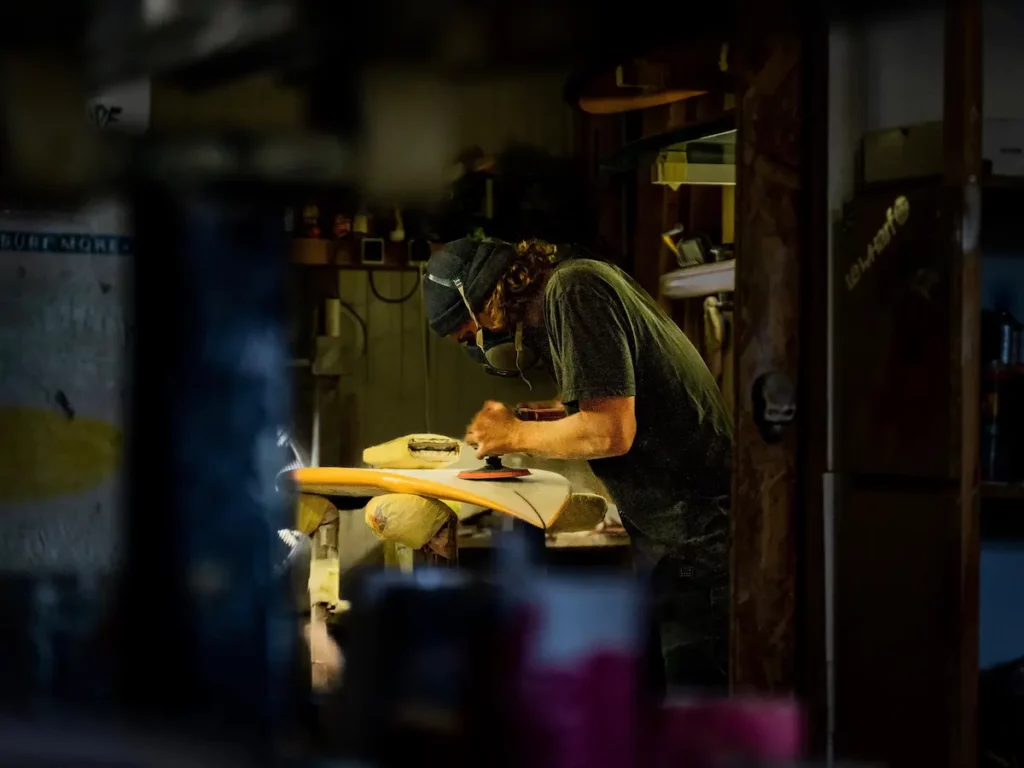 Florian Germain travaillant sur une planche de surf dans son atelier FYGOO à Capbreton, vue de loin